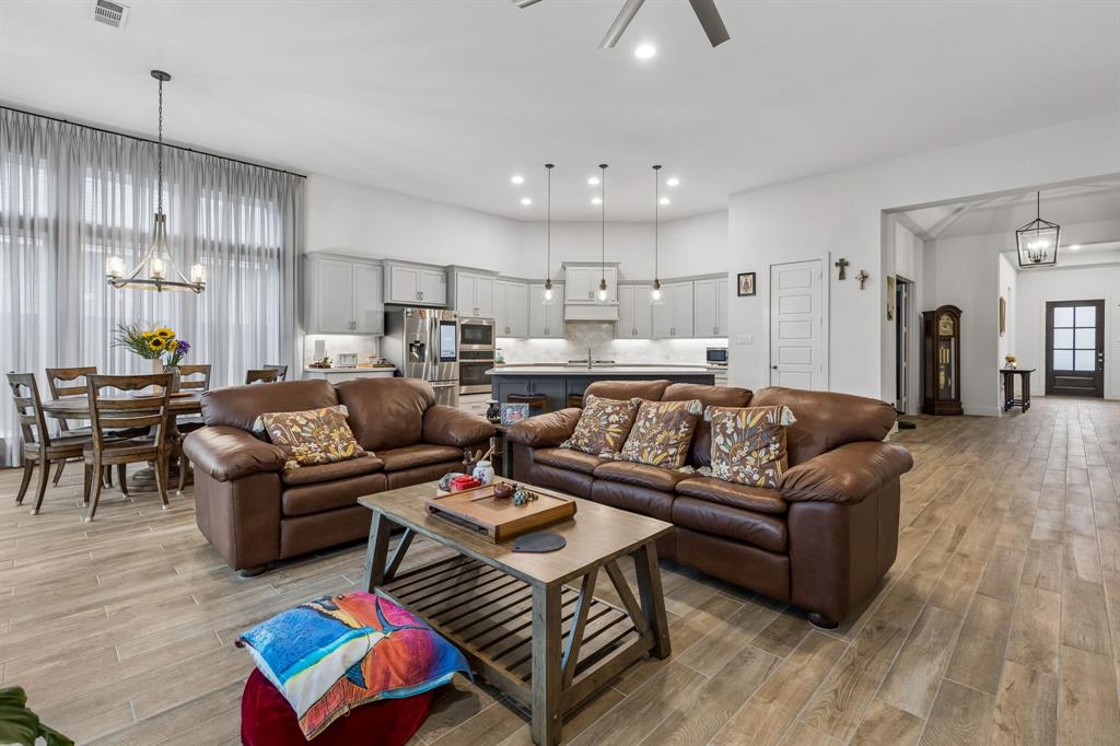 Open-concept interior featuring wood-finish tile flooring, custom cabinetry with a central island, stainless steel built-in appliances, recessed lighting, and multi-pendant illumination