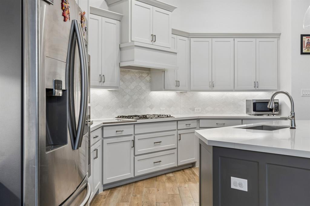 Kitchen featuring white shaker-style cabinetry, a custom range hood, geometric tile backsplash, quartz countertops, and wood-finish flooring