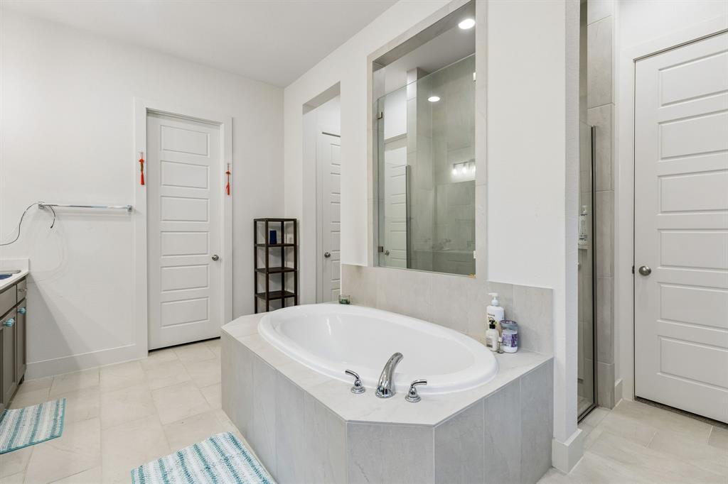 Oval soaking tub with a tiled surround, glass-enclosed shower, polished metal fixtures, and multiple paneled doors