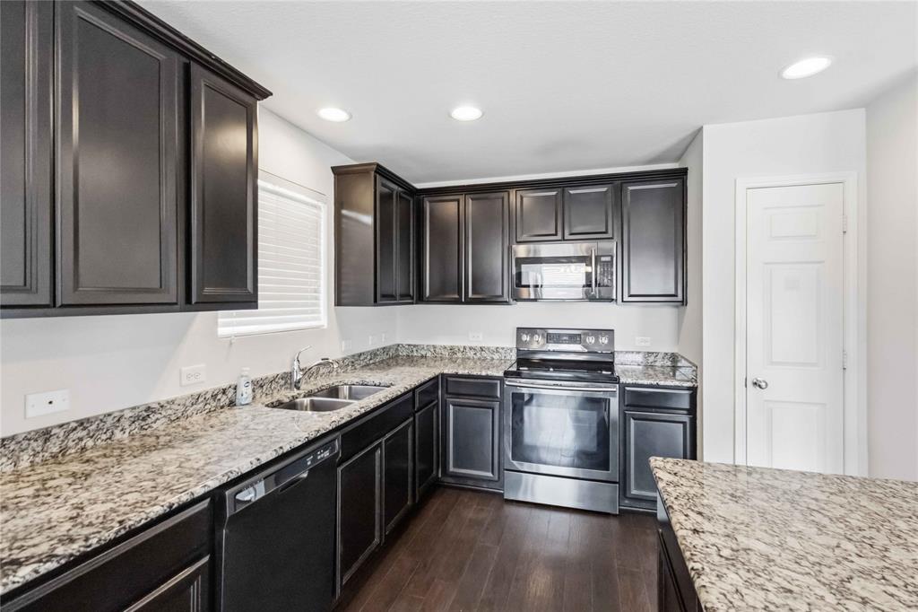 Kitchen featuring espresso-finish cabinetry, stone-patterned countertops, stainless steel appliances, recessed ceiling lighting, and wood-finish flooring