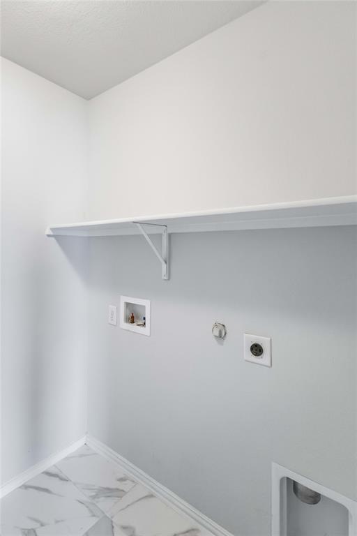 Utility area featuring white-finish walls, stone-look tile flooring, a wall-mounted shelf, and dedicated water and electrical hookups