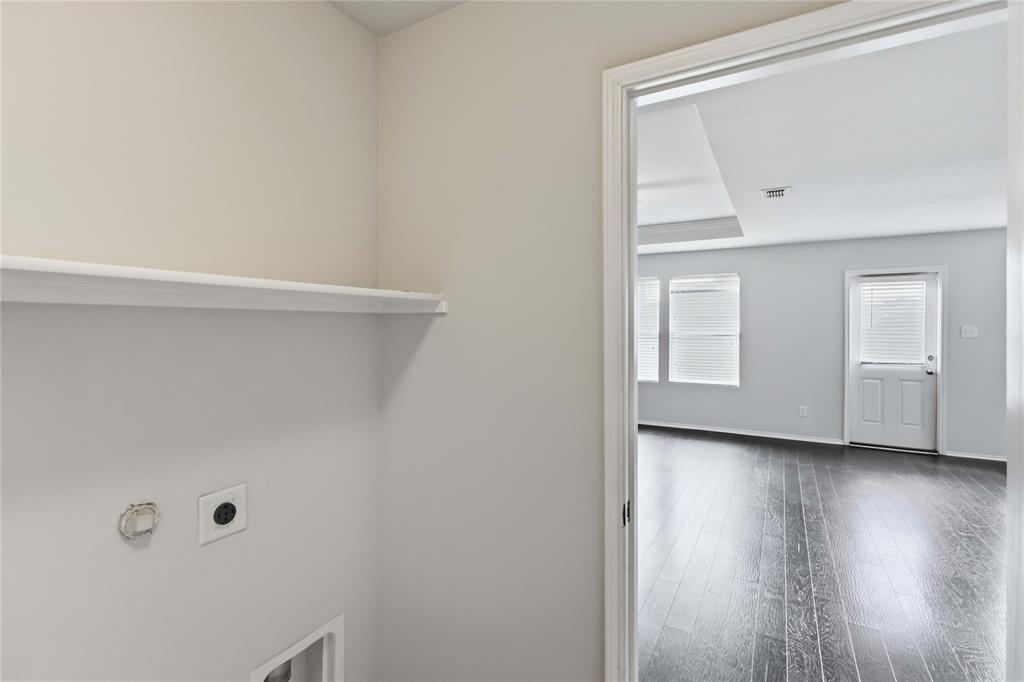 Utility space featuring a built-in shelf and dedicated hookups, highlighting dark-toned wood-finish flooring and an exterior door in the visible room