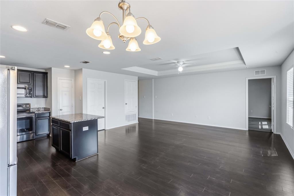 Open-concept space featuring dark wood-finish flooring, a recessed ceiling, a central kitchen island with stone countertop, and a five-light chandelier
