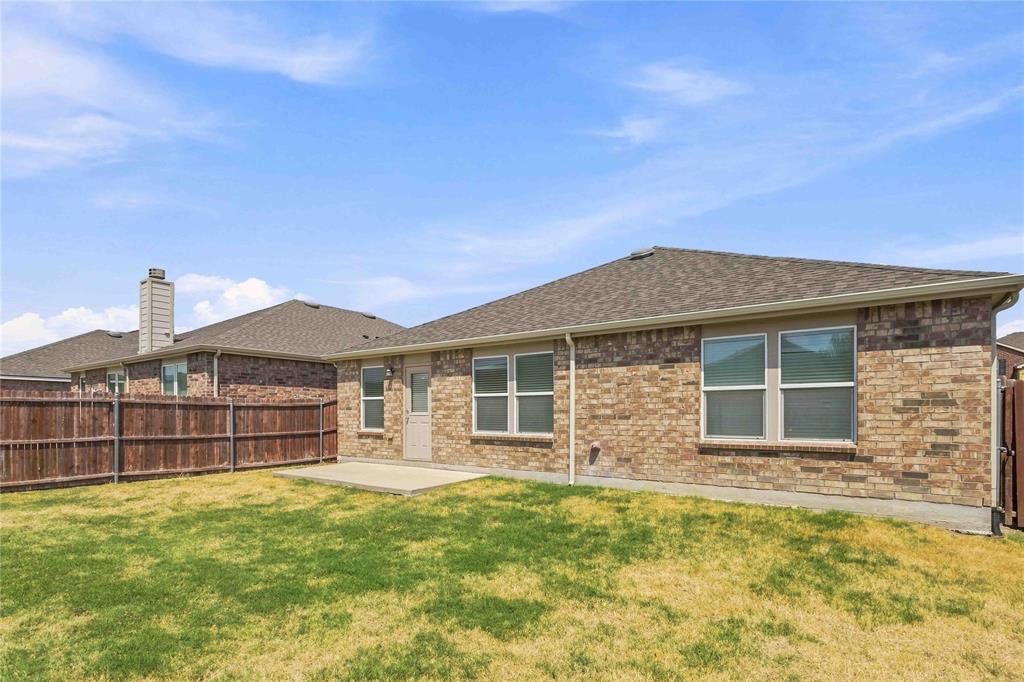 Rear exterior featuring a brick facade, concrete patio, multi-pane windows, and a wood privacy fence