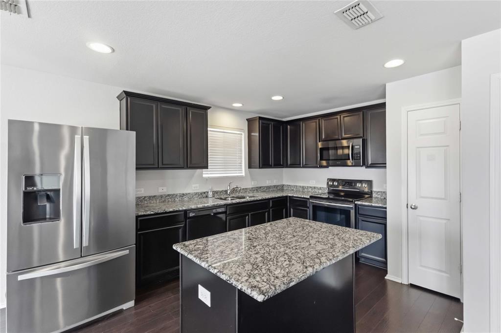 Kitchen featuring dark wood cabinetry, stone countertops, stainless steel appliances, a center island, and wood-finish flooring