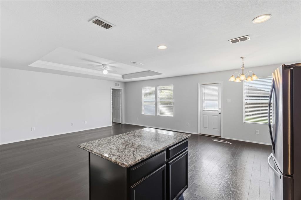 Open-concept living space featuring wood-finish flooring, a tray ceiling with a ceiling fan, a kitchen island with a stone-finish countertop, and recessed lighting
