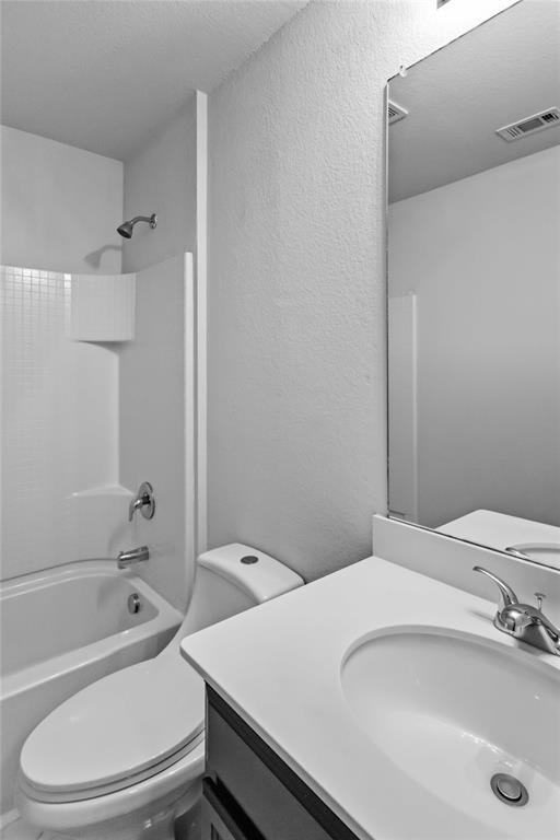 Bathroom featuring a vanity with a white countertop and integrated sink, chrome-finished fixtures, a wall-mounted mirror, and a tub-shower combination with a surround