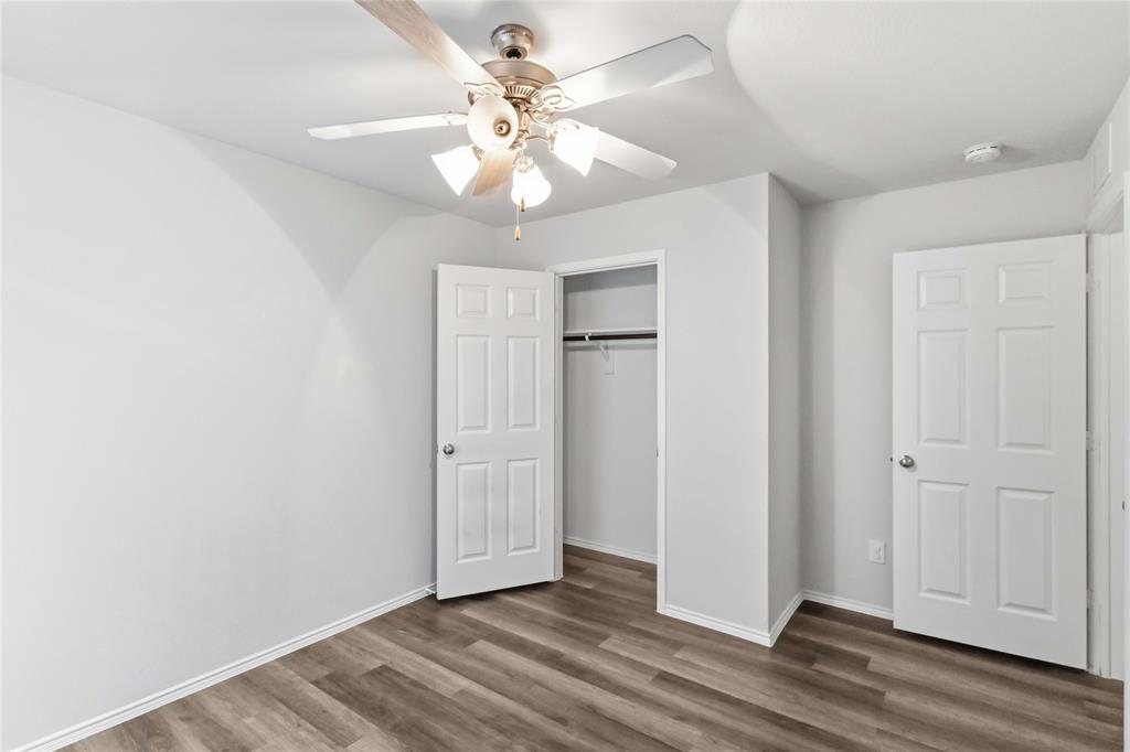 Room featuring wood-finish flooring, a multi-blade ceiling fan with integrated lighting, and six-panel interior doors