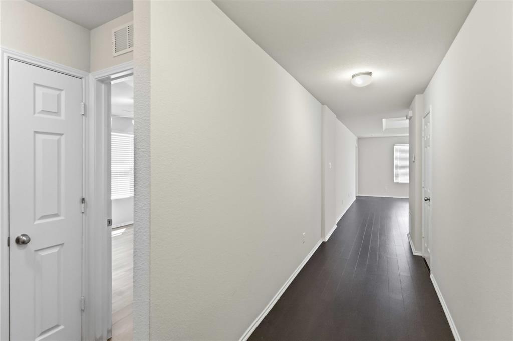 Interior hallway featuring dark wood-finish flooring, neutral wall tones, multi-panel doors, and a ceiling-mounted flush lighting fixture