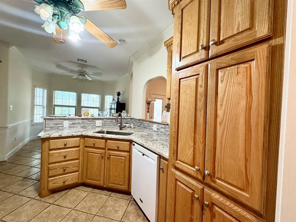 Kitchen featuring wood cabinetry, stone countertops, a mosaic tile backsplash, a stainless steel undermount sink with a pull-down faucet, and tiled flooring Kitchen featuring wood cabinetry, stone countertops, a mosaic tile backsplash, a stainless steel undermount sink with a pull-down faucet, and tiled flooring