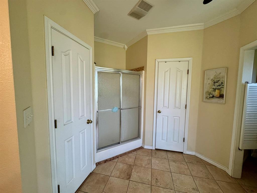 Ceramic tile flooring, crown molding, and a walk-in shower with a metal frame enclosure
