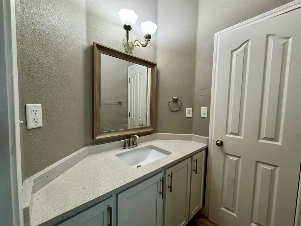 Vanity featuring a light-toned countertop, undermount sink, shaker-style cabinetry, framed wall mirror, and dual-light wall-mounted fixture