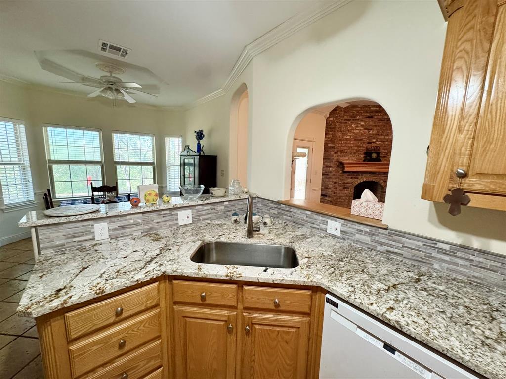 Kitchen featuring stone-finish countertops, mosaic tile backsplash, wood-finish cabinetry, stainless steel sink, and arched wall detailing Kitchen featuring stone-finish countertops, mosaic tile backsplash, wood-finish cabinetry, stainless steel sink, and arched wall detailing