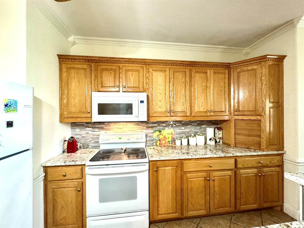 Kitchen featuring wood cabinetry, stone-finish countertops, mosaic tile backsplash, crown molding, and built-in appliance integration Kitchen featuring wood cabinetry, stone-finish countertops, mosaic tile backsplash, crown molding, and built-in appliance integration