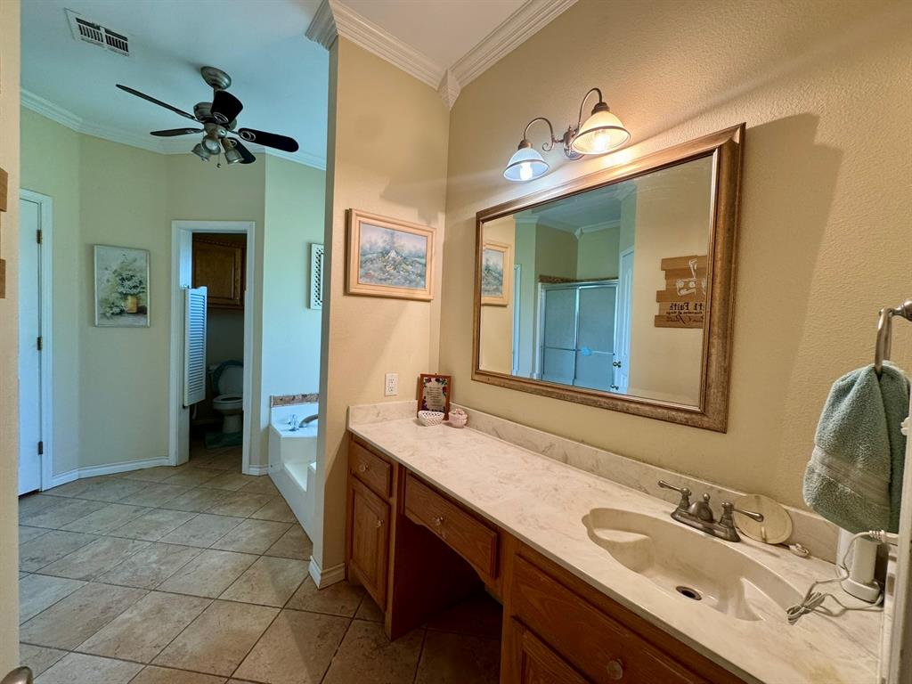 Bathroom featuring a dual-basin vanity with a stone countertop, crown molding, tile flooring, and an integrated bathtub