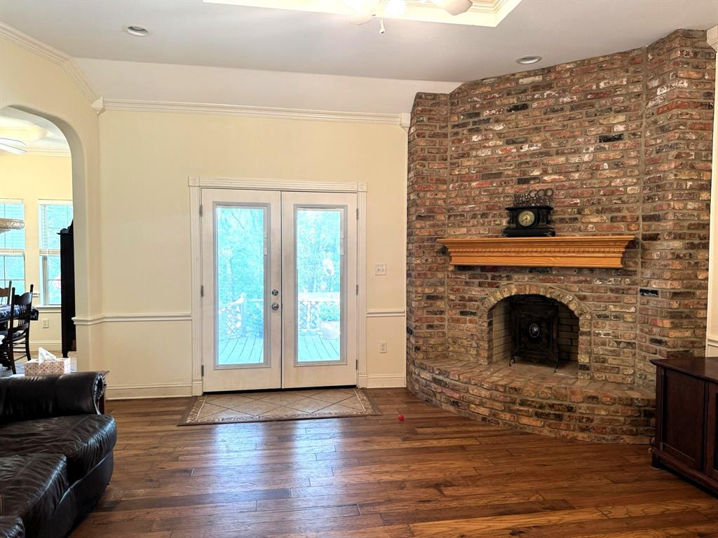 Floor-to-ceiling brick fireplace with an arched firebox and decorative wood mantel, wood-finish flooring, double glass-paneled doors, tray ceiling with recessed lighting, and crown molding