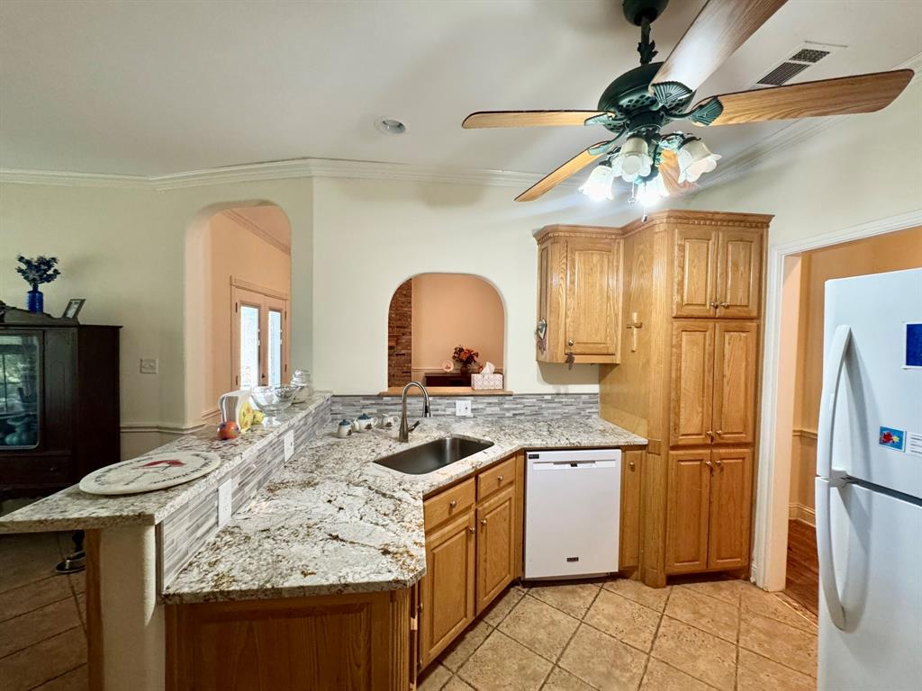 Kitchen featuring stone-finish countertops, tile backsplash, built-in light-tone wood cabinetry, tile flooring, and a ceiling-mounted fan with integrated lighting Kitchen featuring stone-finish countertops, tile backsplash, built-in light-tone wood cabinetry, tile flooring, and a ceiling-mounted fan with integrated lighting