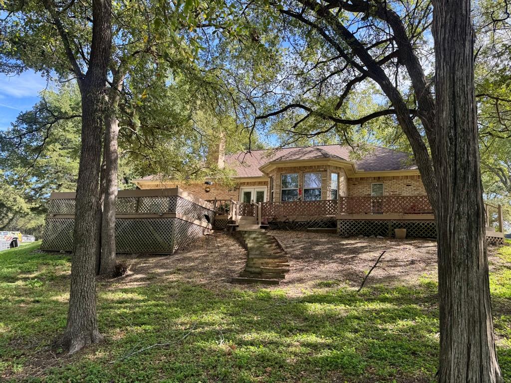 Brick exterior featuring a multi-level wood deck with lattice skirting, stone slab steps, and mature trees