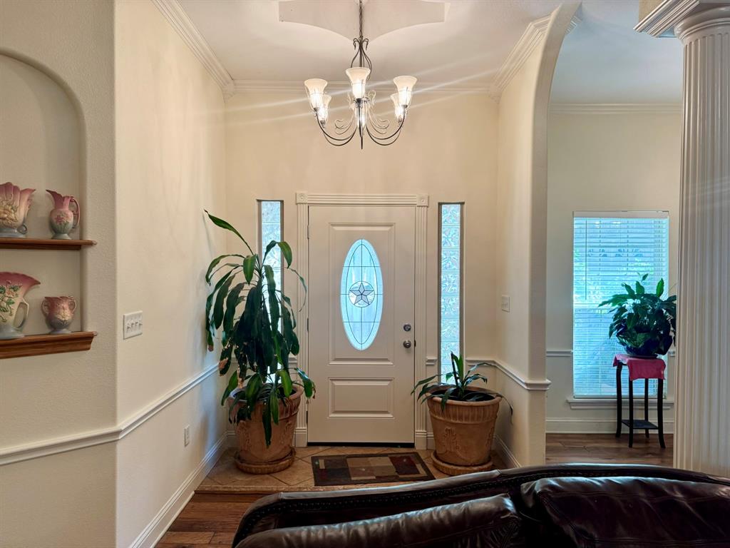 Entryway featuring arched architectural detailing, a central chandelier, decorative wall niche with built-in shelving, fluted column, and white door with oval glass insert flanked by narrow sidelights Entryway featuring arched architectural detailing, a central chandelier, decorative wall niche with built-in shelving, fluted column, and white door with oval glass insert flanked by narrow sidelights