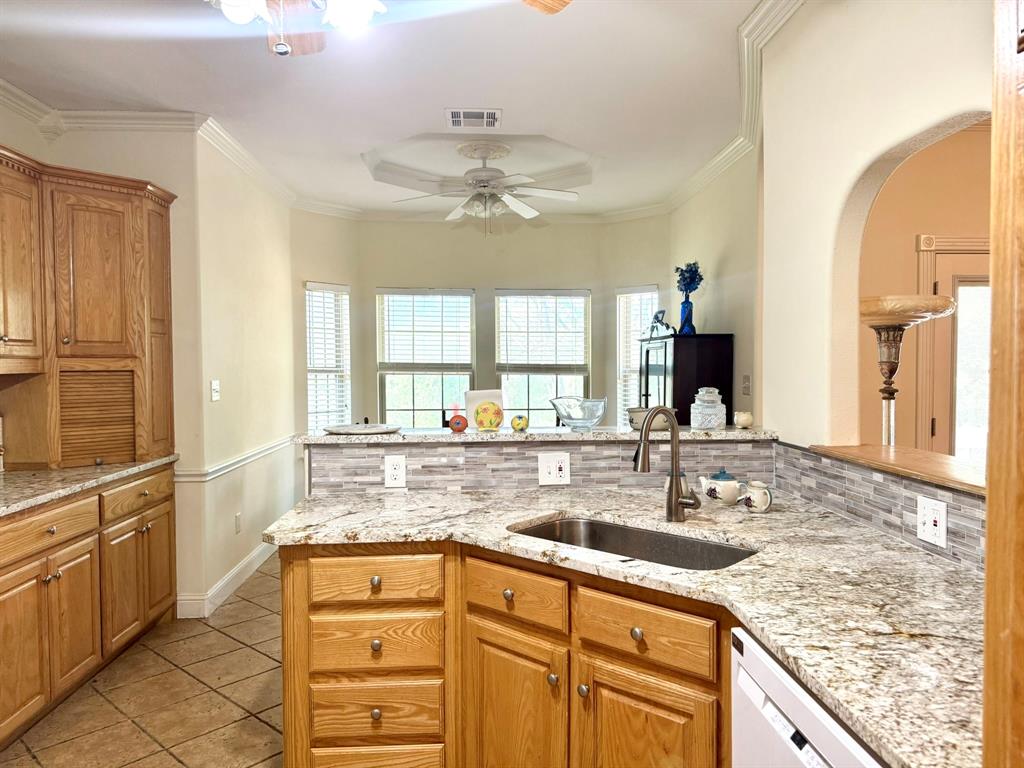 Kitchen featuring stone countertops, tile backsplash, natural finish wood cabinetry, under-mount sink with high-arch faucet, and crown molding Kitchen featuring stone countertops, tile backsplash, natural finish wood cabinetry, under-mount sink with high-arch faucet, and crown molding
