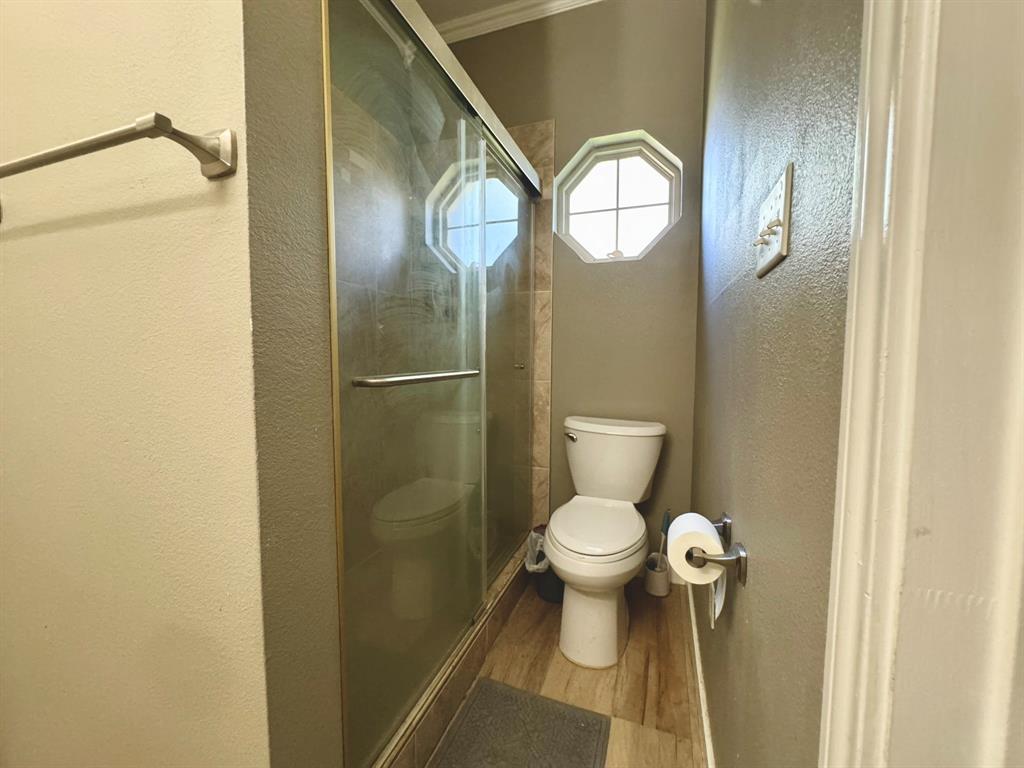 Shower enclosure with a sliding glass door, octagon-shaped window, and wood-finish flooring