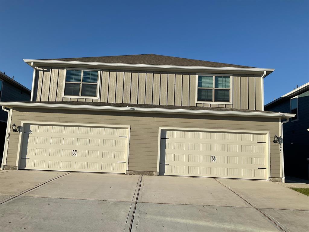 Two-story exterior featuring vertical board-and-batten siding, horizontal lap siding, two individual garage bays, and a concrete driveway