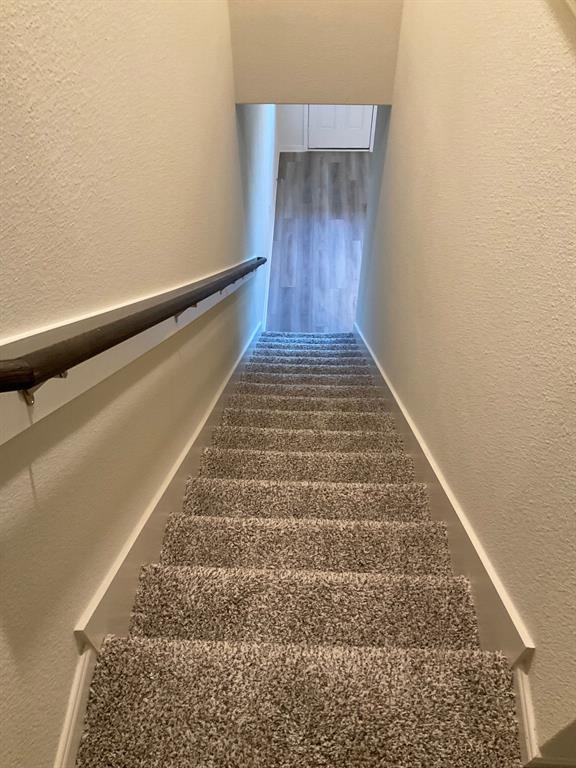 Staircase featuring neutral carpeting, a dark wood-finish handrail, and white walls