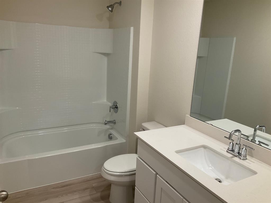 Bathroom featuring a vanity with a white countertop and undermount sink, large wall-mounted mirror, wood-finish flooring, and a shower-tub combination with a white surround