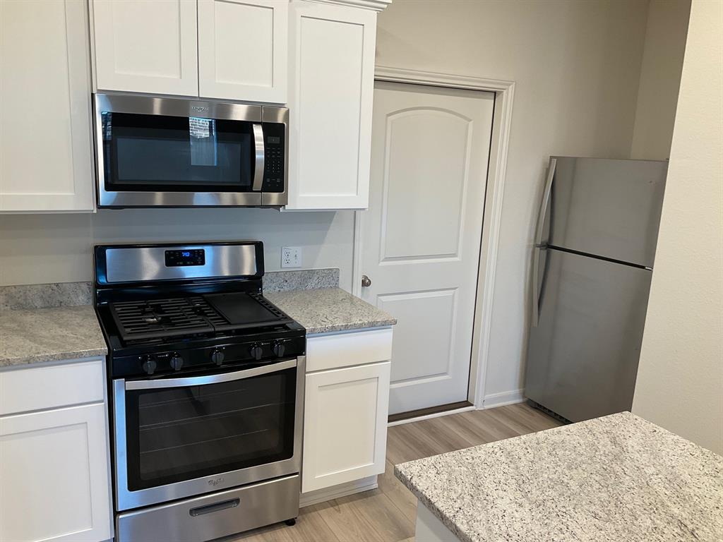 Kitchen featuring white shaker-style cabinetry, stone-finish countertops, stainless steel appliances, and wood-finish flooring