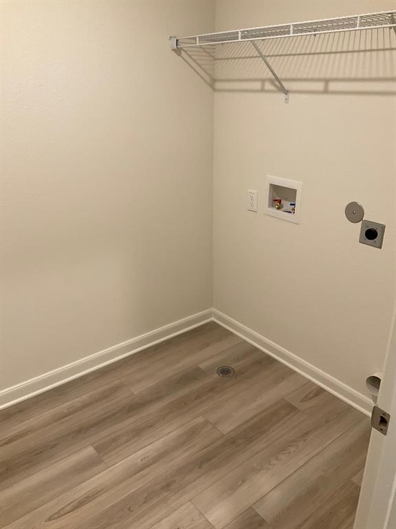 Laundry area featuring wood-finish flooring, a white metal shelving unit, and dedicated utility hookups