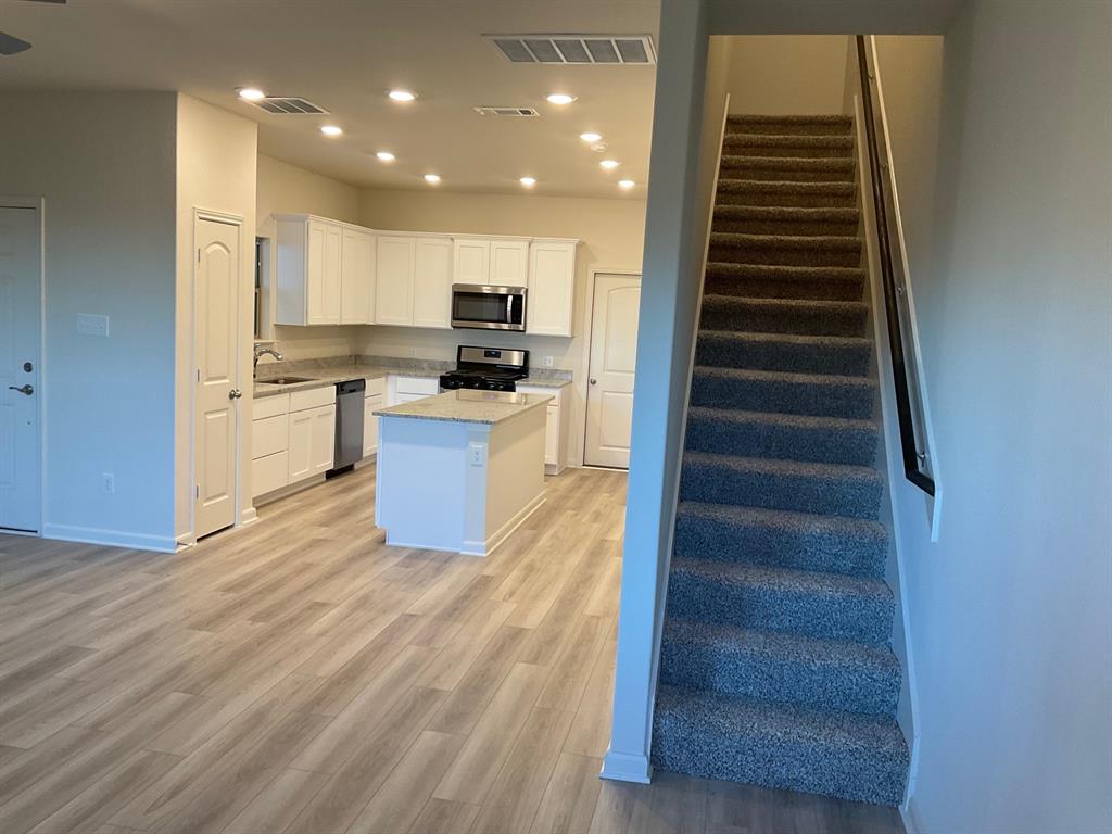 Kitchen featuring white shaker-style cabinetry, central island, stone-finish countertops, recessed lighting, and wood-finish flooring