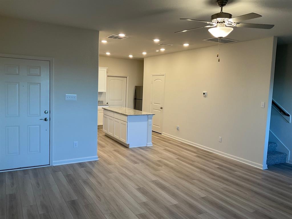 Open-concept interior featuring wood-finish flooring, recessed lighting, a ceiling fan, and a kitchen island with stone-finish countertops