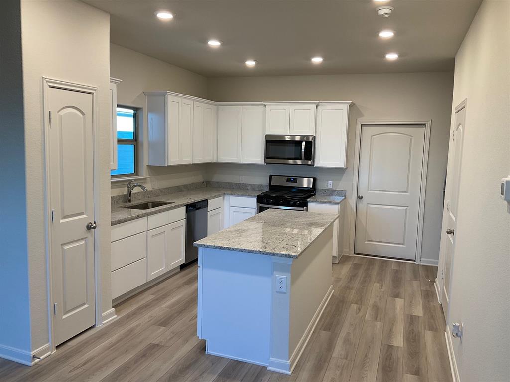 Kitchen featuring white shaker-style cabinetry, stone-surface countertops, central island, stainless steel appliances, and wood-finish flooring