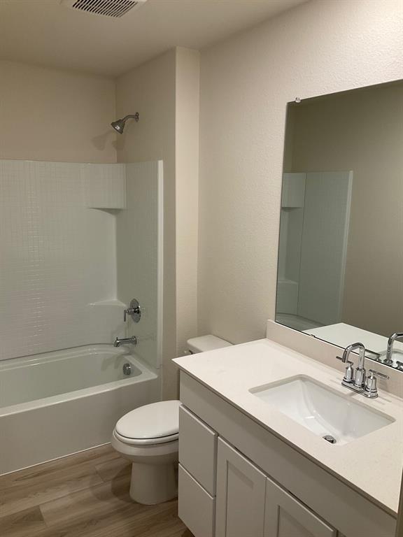 Bathroom featuring white cabinetry, a solid-surface countertop with an integrated basin, a large wall-mounted mirror, wood-finish flooring, and a tub-shower combination with a tiled surround