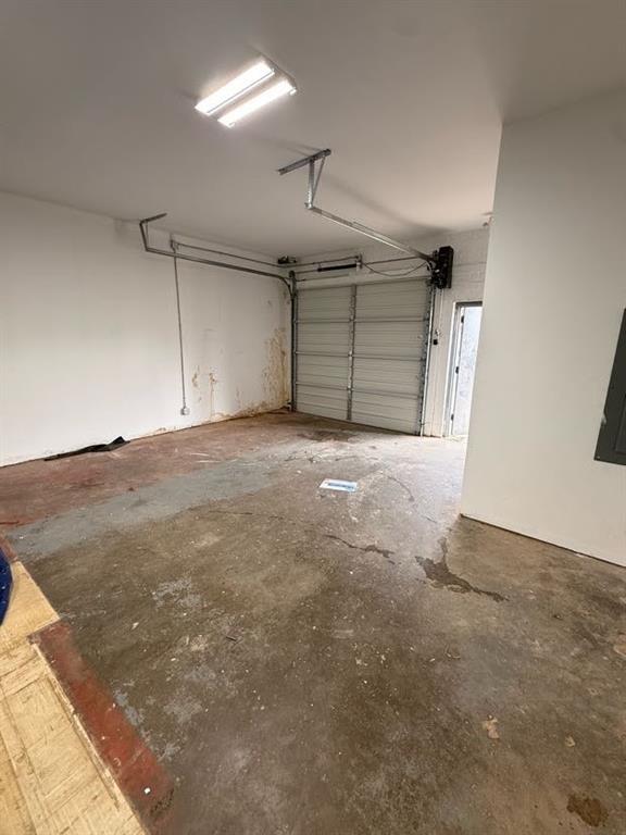 Enclosed garage featuring a metal sectional door, concrete flooring, overhead fluorescent lighting, and a pedestrian access door