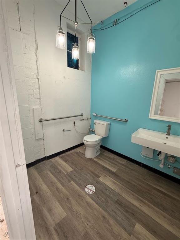 Wall-mounted sink with a single-handle faucet, wood-finish flooring, three-light hanging pendant fixture, and stainless steel grab bars