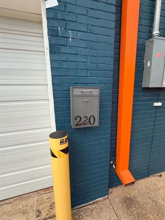 Painted brick exterior wall featuring a metal wall-mounted mailbox, high-visibility safety bollard, and integrated gutter system