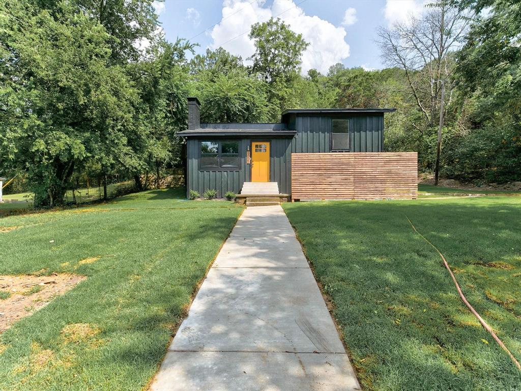 Modern exterior featuring vertical metal siding, horizontal wood-slat privacy screening, a prominent chimney stack, and a concrete walkway