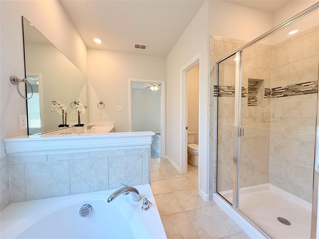 Bathroom featuring a soaking tub with tile surround, a separate glass-enclosed shower with decorative inlay, a large wall-mounted mirror, and tile flooring