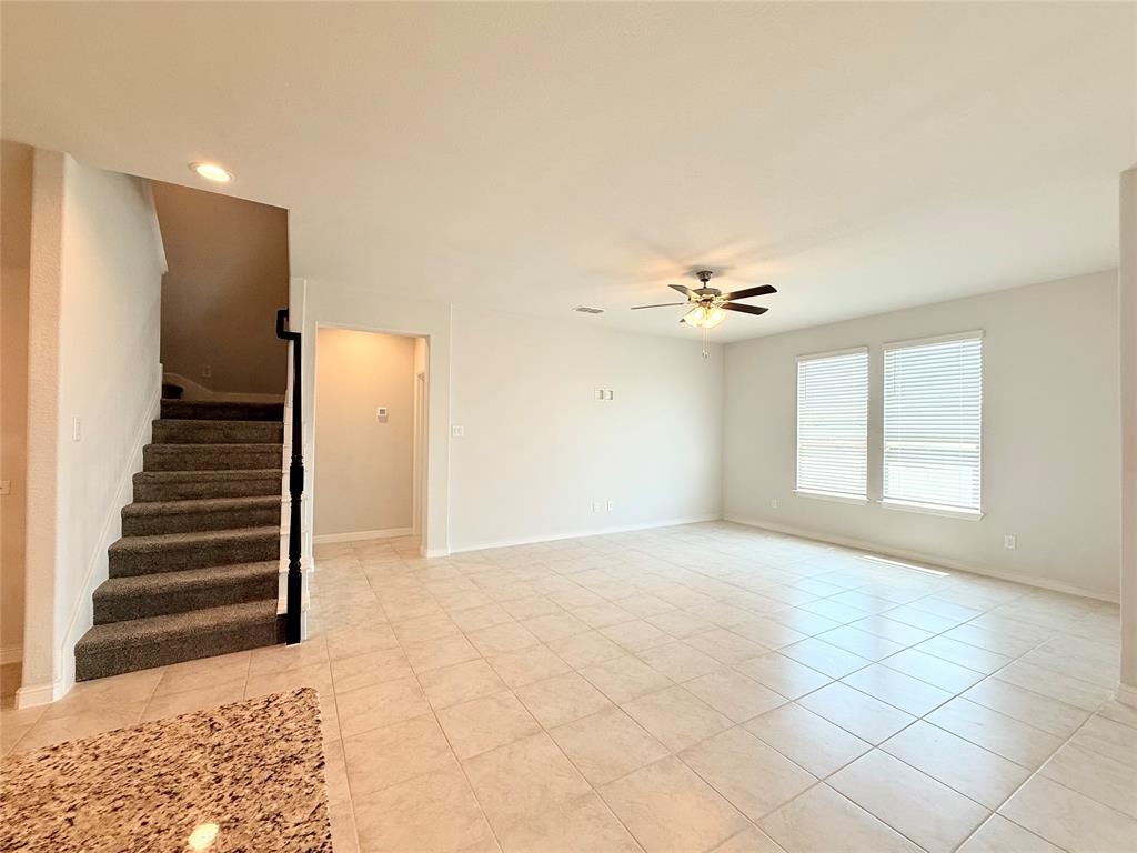 Open interior space featuring light-toned tile flooring, recessed ceiling lighting, a multi-blade ceiling fan, and a staircase with carpeted treads