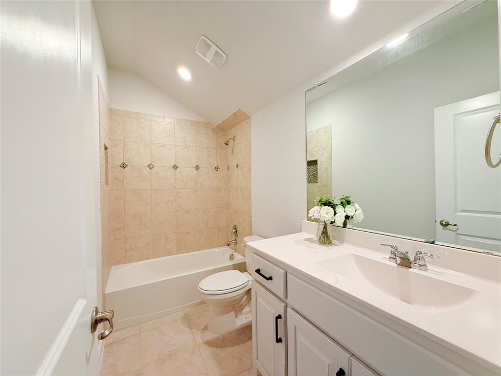 Bathroom featuring a vanity with a white countertop and rectangular undermount sink, white cabinetry with matte black hardware, a large wall-mounted mirror, and a tub-shower combination with tile surround and inset niche