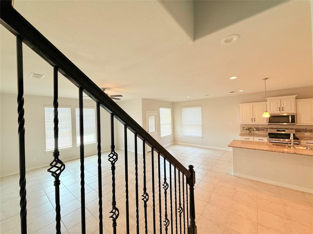 Staircase featuring black decorative iron balusters, tile flooring, kitchen with white cabinetry, granite countertops, and recessed lighting