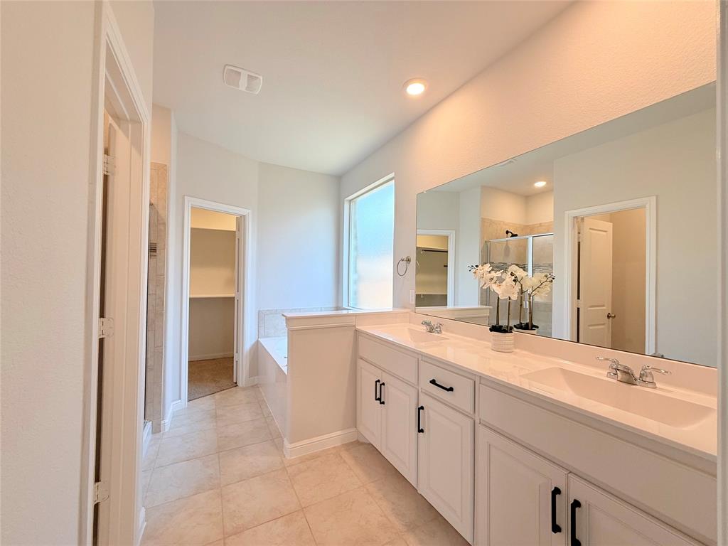Double vanity with white cabinetry, stone-finish countertops, rectangular integrated sinks, and matte black hardware, featuring a full-width mirror and tile flooring