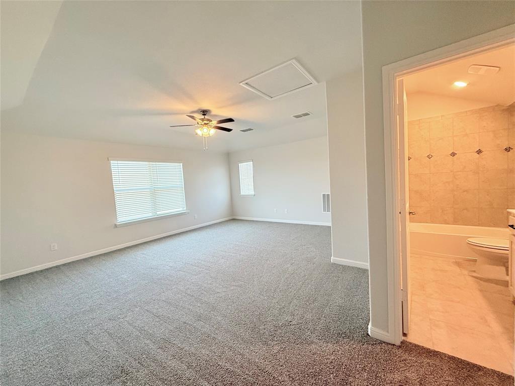 Spacious room featuring carpeting, a ceiling fan, and large windows, with an attached bathroom showcasing a tiled shower enclosure and light-toned flooring