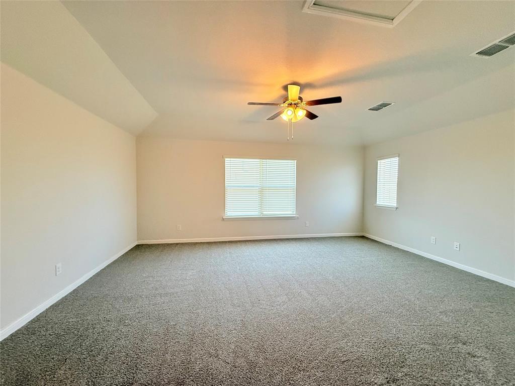 Spacious room featuring neutral carpeting, vaulted ceilings, multi-pane windows with blinds, and a ceiling fan with integrated lighting