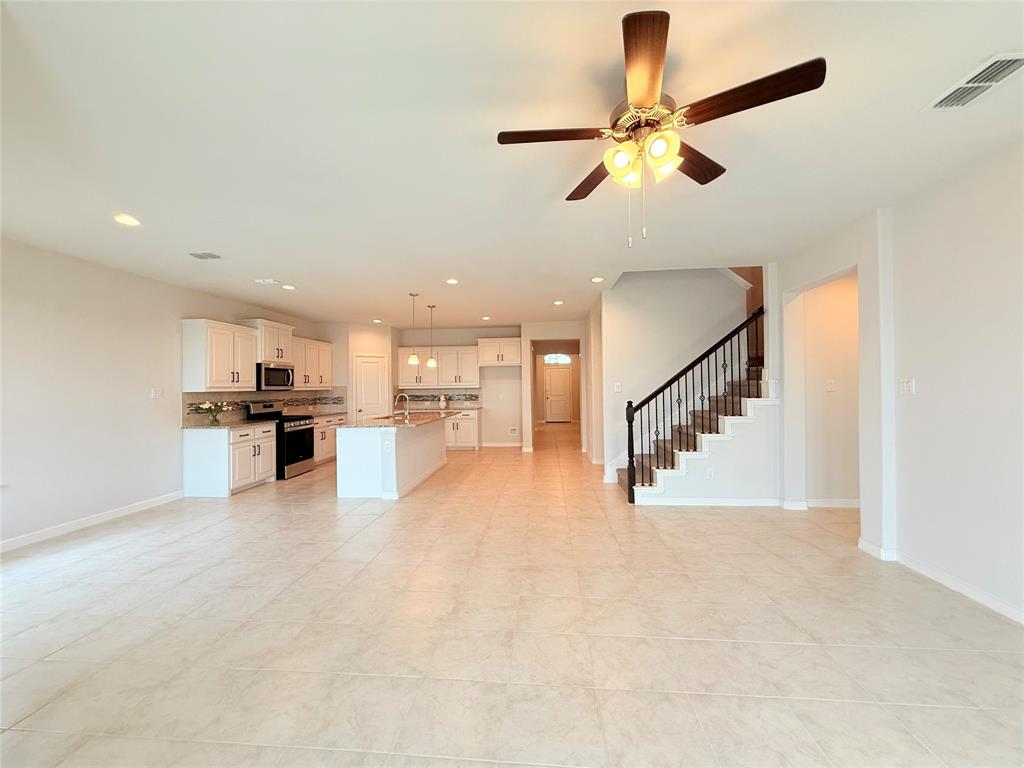 Open-concept interior featuring light-toned tile flooring, white cabinetry, a kitchen island, recessed lighting, and a staircase with metal balusters
