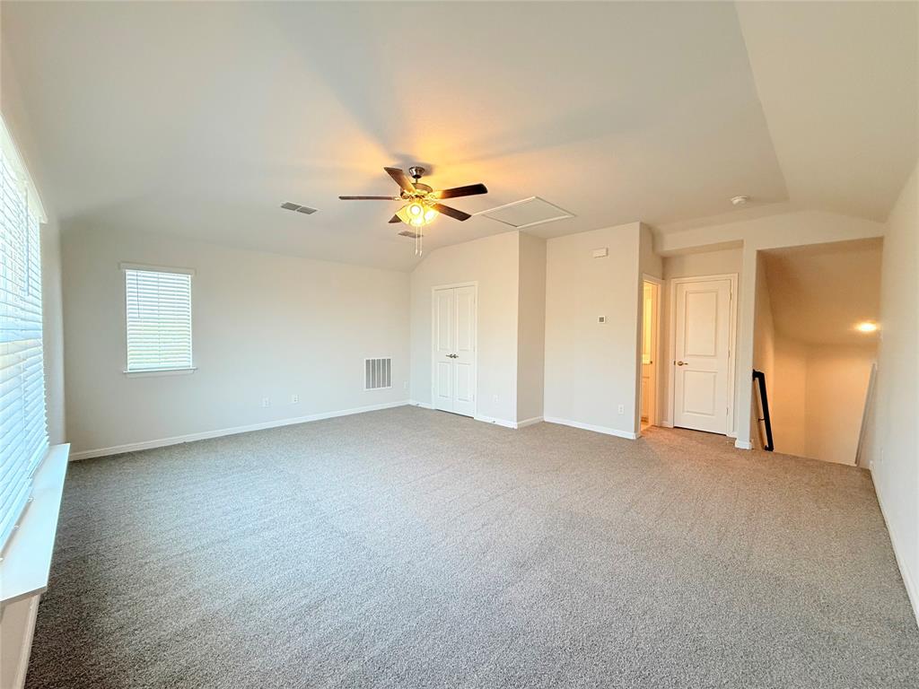 Expansive room featuring neutral carpeting, vaulted ceilings, a central multi-blade ceiling fan with integrated lighting, and white interior doors