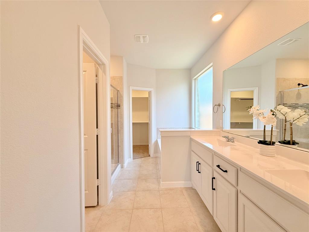 Double vanity with light-toned countertops, white shaker-style cabinetry featuring matte black hardware, tile flooring, and a large wall-mounted mirror