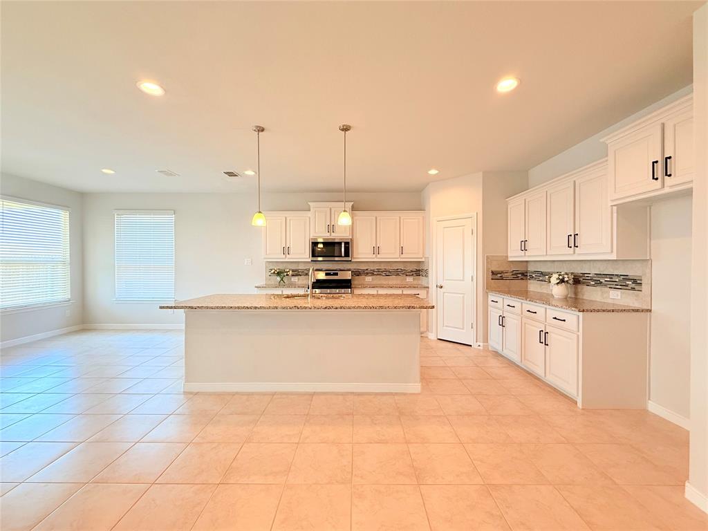Kitchen featuring white shaker-style cabinetry, stone-finish countertops, tile backsplash, a center island with pendant lighting, and tile flooring