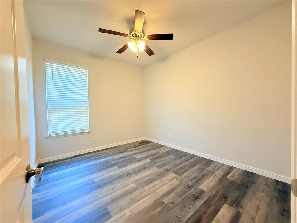 Room featuring wood-finish flooring, a ceiling fan with integrated lighting, and a window with blinds
